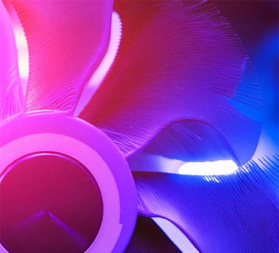 Nahaufnahme eines leuchtenden Computerlüfters in Bewegung, der eine Mischung aus Rosa- und Lilatönen zeigt. Die Flügel sind beleuchtet und erzeugen ein sanftes Leuchten, das ihre geschwungene Form und das Muster aus Licht und Schatten hervorhebt.